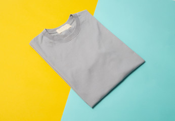 Grey folded t-shirt isolated on yellow and blue background.