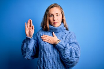 Young beautiful blonde woman wearing casual turtleneck sweater over blue background Swearing with...