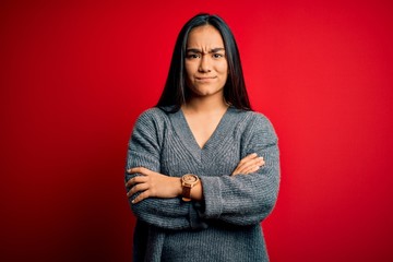 Young beautiful asian woman wearing casual sweater standing over isolated red background skeptic and nervous, disapproving expression on face with crossed arms. Negative person.