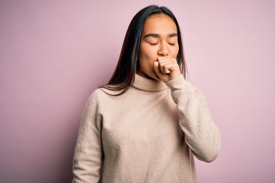Young beautiful asian woman wearing casual turtleneck sweater over pink background feeling unwell and coughing as symptom for cold or bronchitis. Health care concept.