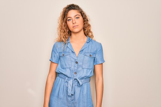 Young beautiful woman with blue eyes wearing casual denim dress over white background Relaxed with serious expression on face. Simple and natural looking at the camera.