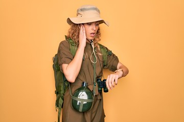 Young blonde explorer woman with blue eyes hiking wearing backpack and water canteen Looking at the watch time worried, afraid of getting late