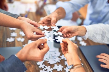 Group of business workers with hands together connecting pieces of puzzle at the office