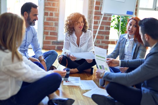 Group of business workers smiling happy and confident. Sitting on the floor relaxed working together speaking and reading documents at the office