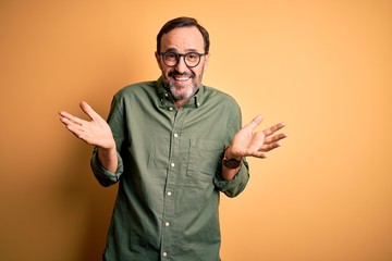 Middle age hoary man wearing casual green shirt and glasses over isolated yellow background...