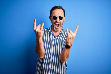 Middle age hoary man wearing striped shirt and sunglasses over isolated blue background shouting...