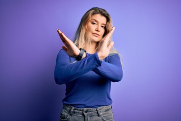 Young beautiful blonde woman wearing casual t-shirt over isolated purple background Rejection expression crossing arms doing negative sign, angry face