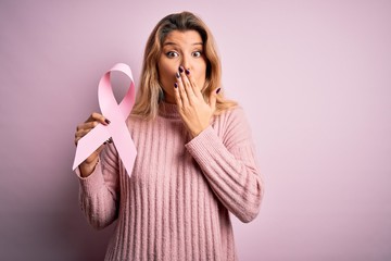 Young beautiful blonde woman asking for support cancer holding pink ribbon symbol cover mouth with hand shocked with shame for mistake, expression of fear, scared in silence, secret concept
