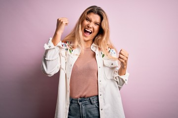 Young beautiful blonde woman wearing casual jacket standing over isolated pink background celebrating surprised and amazed for success with arms raised and open eyes. Winner concept.