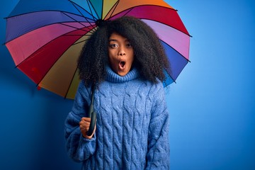 Young african american woman with afro hair under colorful umbrella for winter weather rain scared...
