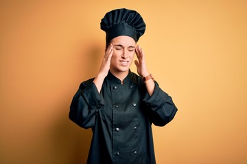 Young beautiful chef woman wearing cooker uniform and hat standing over yellow background with hand on headache because stress. Suffering migraine.