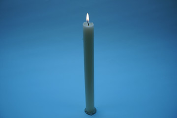 Lit candle close-up on a blue background.
