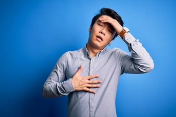 Young handsome chinese man wearing casual shirt standing over isolated blue background Touching...