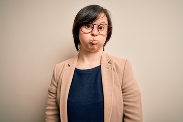 Young down syndrome business woman wearing glasses standing over isolated background puffing cheeks with funny face. Mouth inflated with air, crazy expression.