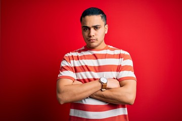 Young brazilian man wearing casual striped t-shirt standing over isolated red background skeptic...