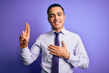 Young brazilian businessman wearing elegant tie standing over isolated purple background smiling swearing with hand on chest and fingers up, making a loyalty promise oath