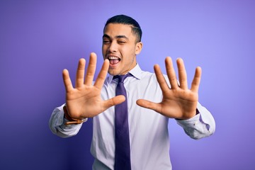 Young brazilian businessman wearing elegant tie standing over isolated purple background showing and pointing up with fingers number ten while smiling confident and happy.