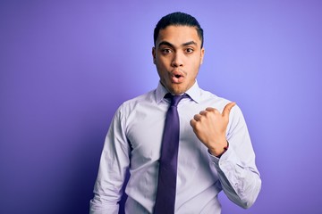 Young brazilian businessman wearing elegant tie standing over isolated purple background Surprised pointing with hand finger to the side, open mouth amazed expression.
