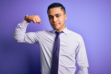Young brazilian businessman wearing elegant tie standing over isolated purple background Strong person showing arm muscle, confident and proud of power