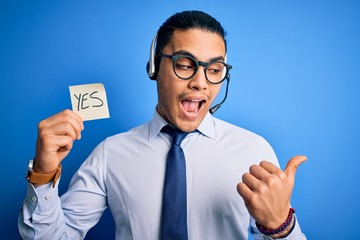 Young brazilian call center agent man holding reminder paper with yes message pointing and showing...