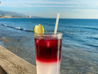 Glass of ice-cooled colorful red margarita cocktail in front of the sea. Holiday concept