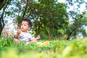Adorable asian preschooler boy playing in summer park sittingon the grass