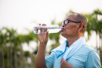A happy old asian man is drinking water at park with sunlight. Healthcare and senior sports concept.