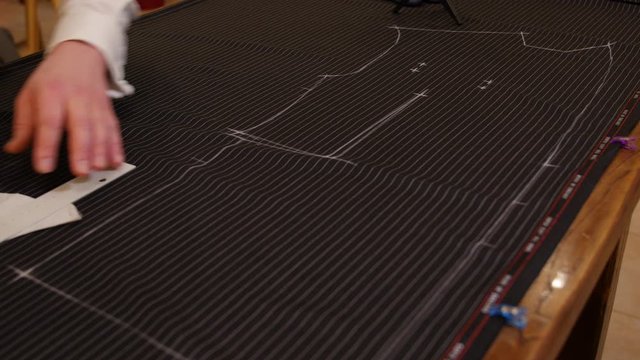 Serious tailor hands drawing on wooden table in amazing atelier the pattern of a made to measure suit. Young attractive fashion designer working in studio