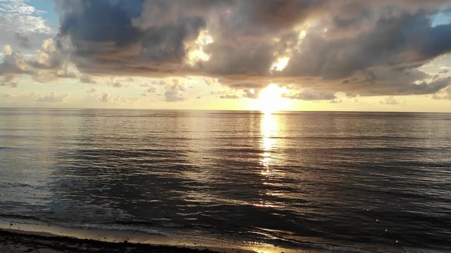 Slowly elevating drone shot of calm ocean waters with clouds and sunrise