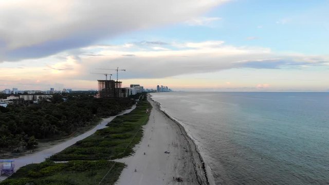 Slow aerial pan from calm ocean to reveal shoreside town in Miami Beach with construction in the distance