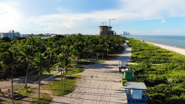 Gentle elevation drone shot of Miami Beach side town with construction in background and sand tracks, palm trees in foreground.
