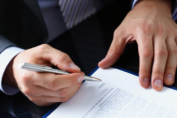Male arm in suit and tie fill form clipped to pad with silver pen closeup. Sign gesture read pact sale agent bank job make note loan credit mortgage investment finance chief legal law concept