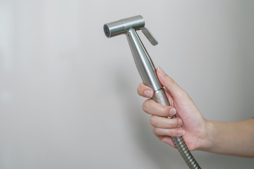 Woman hand using Chromium bidet shower sitting on toilet.