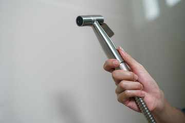 Woman hand using Chromium bidet shower sitting on toilet. - obrazy, fototapety, plakaty