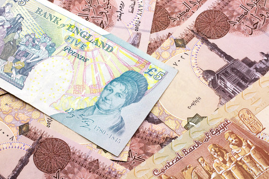A close up image of a multicolored five pound note from the United Kingdom on a background of Egyptian one pound bank notes in macro