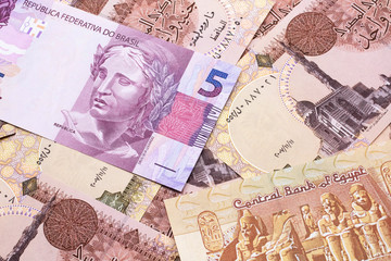 A pink five reais bank note from Brazil close up in macro with a background of Egyptian pound bills
