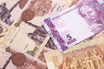 A pink five reais bank note from Brazil close up in macro with a background of Egyptian pound bills
