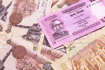 A close up image of a pink, ten taka bank note from Bangladesh on a bed of Egyptian one pound bank notes in macro