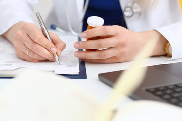 Female medicine doctor hand hold jar of pills and write prescription to patient at worktable. Panacea and life save prescribing treatment legal drug store concept. Empty form ready to be used