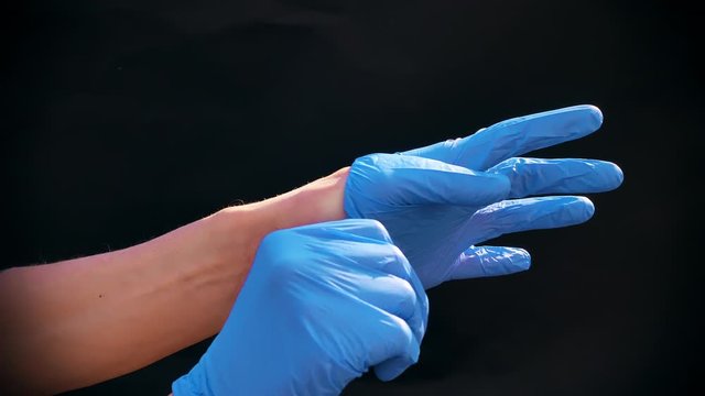 The hands of a Caucasian man wear blue medical gloves. Black background.Preparing a doctor for an operation or medical procedure.