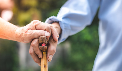 Close up of elderly hands in wrinkles holding walking stick.elderly old man with walking stick stand on footpath sidewalk crossing.