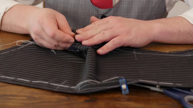 Unrecognisable man tailor hands stitch up cloth with basting tread a jacket of high english fabric. this tailoring process is done on dark grey / black pinstriped wool suit cloth.