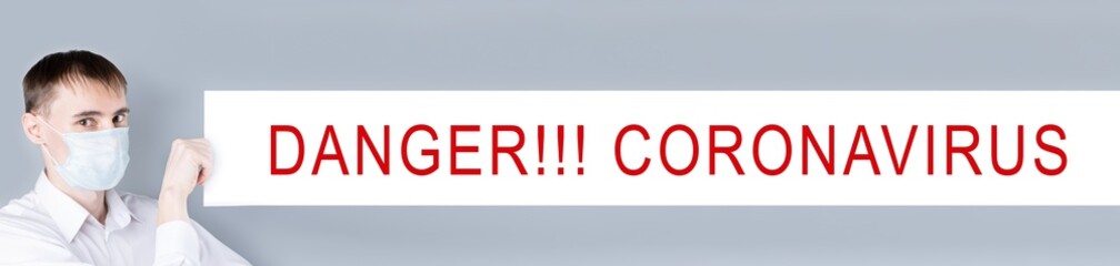 Banner. A very long banner. Man in a medical mask. A man in a white shirt, looks at the camera and holding  a very long blank sheet of paper, with the text danger coronavirus.