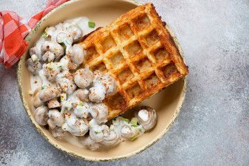 Close-up of belgian potato waffle served with roasted champignons, above view on a beige stone background