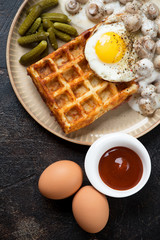 Potato waffle served with mushrooms, fried egg and pickles on a beige plate, vertical shot, flatlay