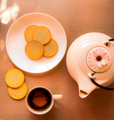 Good morning. The kettle and  a cup of a tea, cookies and a plate with cookies on the wooden table.
