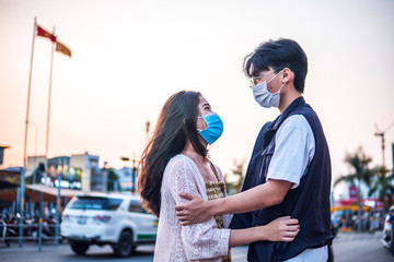 Young millennials couple hugging and wearing a protective face mask, virus spread prevention and people concept