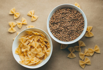 Dry pasta and buckwheat in white ceramic bowls, ingredients for making breakfast or lunch