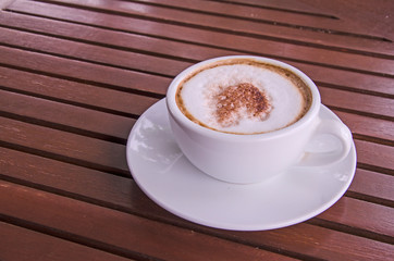 White ceramic cup of coffee in small dish on brown floor