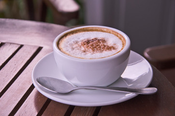 White ceramic cup of coffee and small dish on brown floor